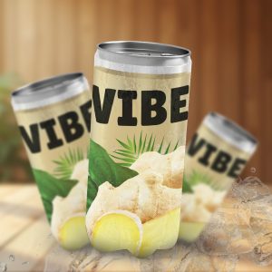 Trois canettes de boisson VIBE sur une table en bois avec de la végétation en arrière-plan. La canette principale est beige avec des feuilles de palmier, une tranche de citron et du gingembre sur l'étiquette. C'est une maquette publicitaire.