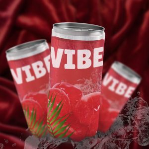 Trois canettes de boisson VIBE sur un fond de tissu rouge. Les canettes sont rouges, avec des cerises et une feuille de palmier sur l'étiquette. On aperçoit des glaçons et des éclaboussures d'eau à leurs pieds. L'image est une maquette publicitaire.